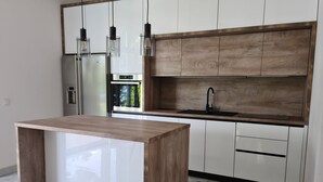 A modern kitchen with a central island, wooden cabinets, a black sink, and pendant lighting. - House Pine Tree (Omis)