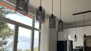 A modern kitchen with a large dining table, hanging pendant lights, and a view of the outdoors. - House Pine Tree (Omis)