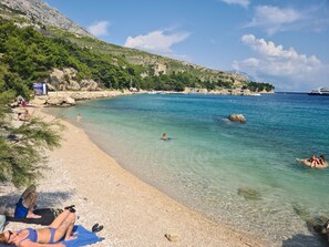 A beach with clear water, rocky shore, and a boat in the distance. - House Pine Tree (Omis)