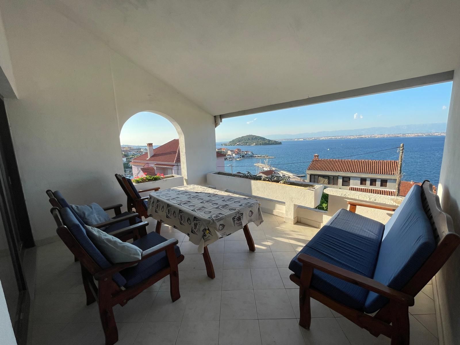 A balcony with a table and chairs, overlooking a coastal view with buildings and a body of water.