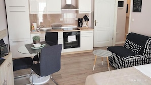 A compact kitchen with white cabinets, a dining table with chairs, a small round table, and a black and white patterned sofa. - Apartment Fiume (Rijeka)