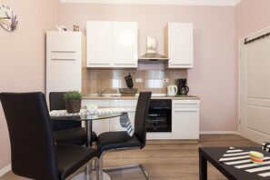 A compact kitchen with white cabinets, a stainless steel range hood, a coffee maker, and a dining area with a glass table and black chairs. - Apartment Fiume (Rijeka)