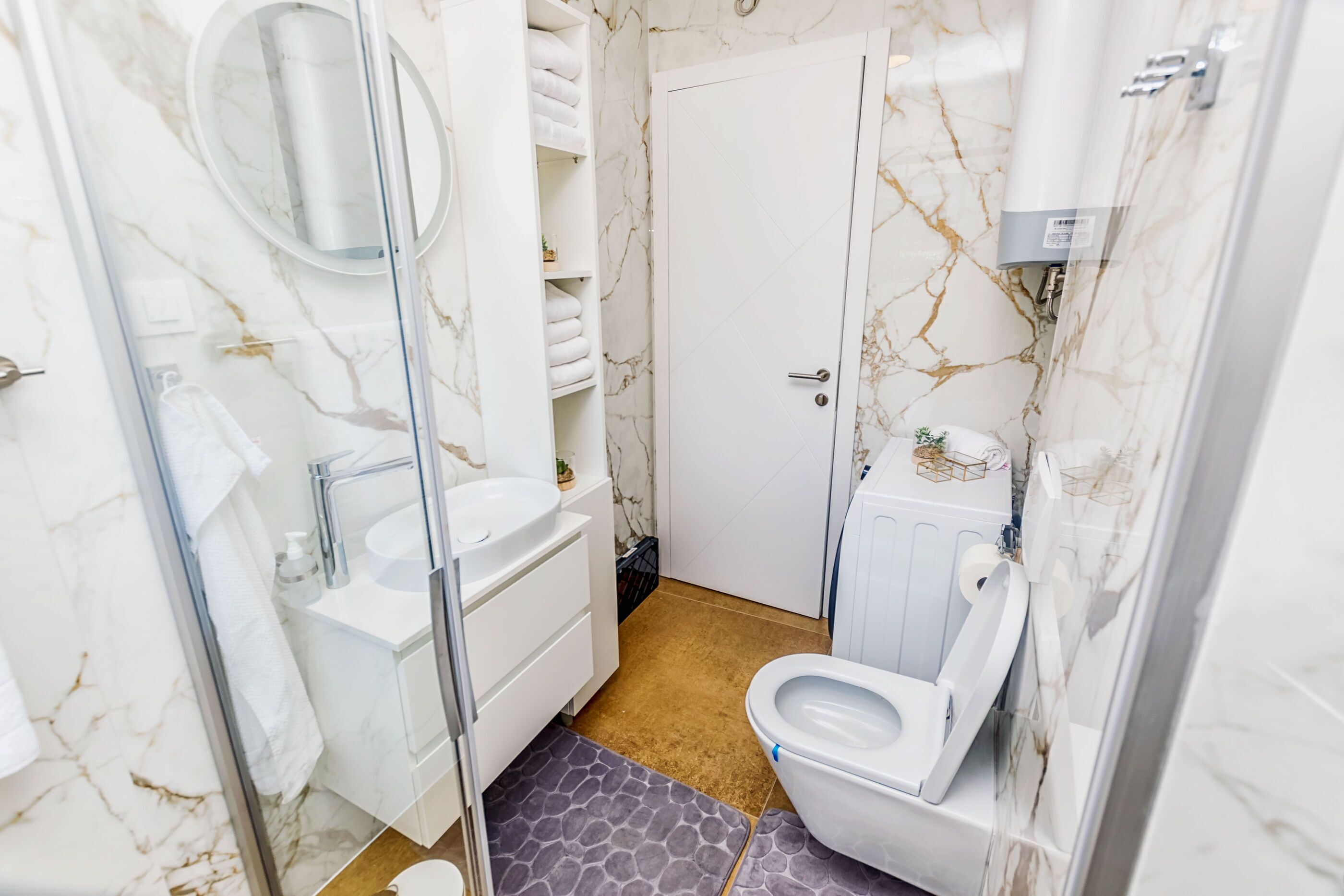 Un bagno con parete in marmo, lavabo bianco, WC e cabina doccia in vetro.