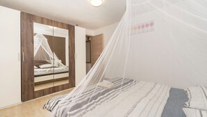 Ein Schlafzimmer mit einem Bett, das unter einem Moskitonetz hängt, einem Kleiderschrank mit Spiegel und einem Nachttisch.