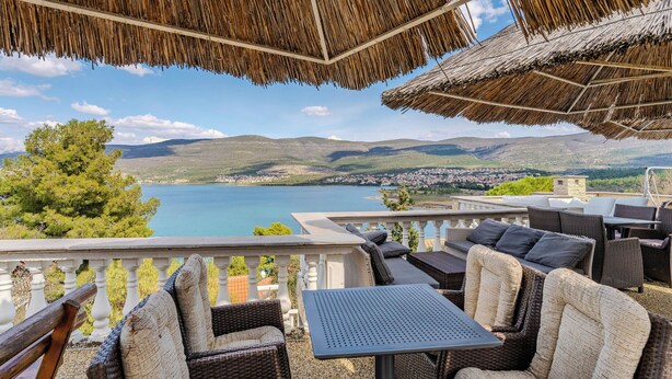 Eine Terrasse mit Korbmöbeln und Blick auf einen See und Hügel.