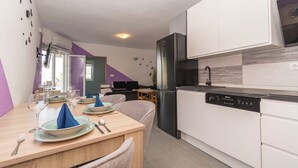 Eine moderne Küche mit weißen Schränken, einem schwarzen Kühlschrank und einem Geschirrspüler. Ein Esstisch ist gedeckt mit Tellern, Gläsern und Besteck.