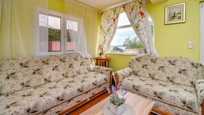 A living room with two sofas, a small table with a vase, a window with curtains, and a painting on the wall. - Apartment Sweet (Marina)