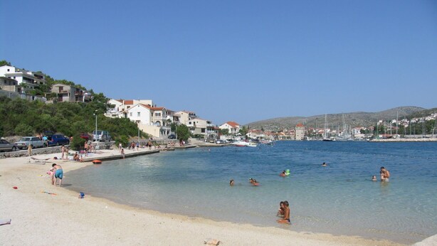 A beach with clear water, people swimming and sunbathing, and buildings in the background. - Apartment Sweet (Marina)