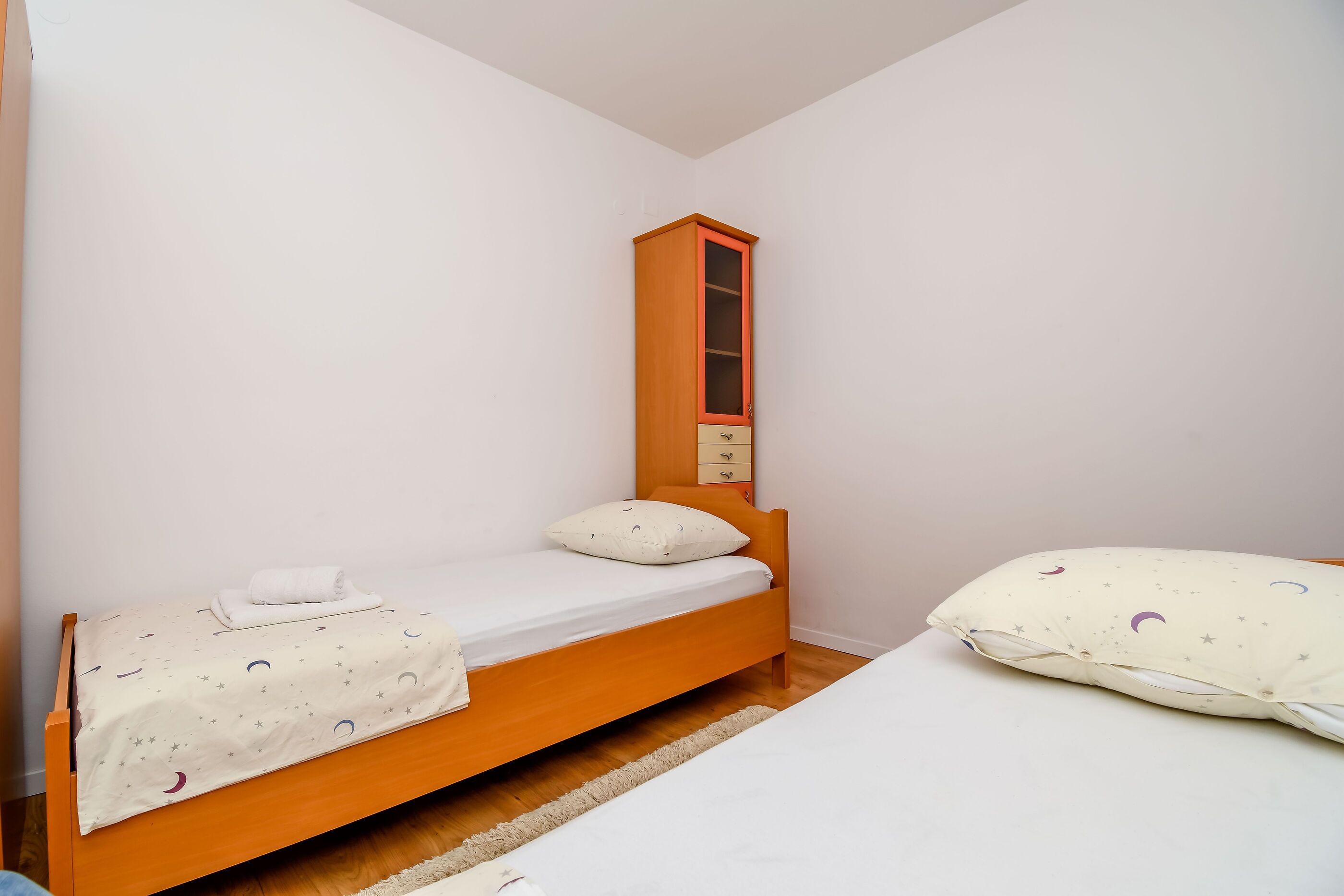 A small, single-bed room with a wooden bed frame, a nightstand, and a wardrobe with a mirror.