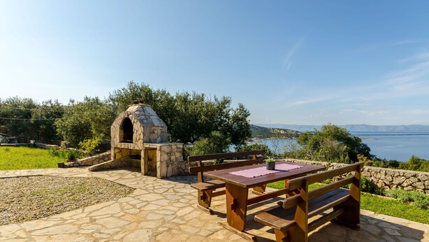 An outdoor patio with stone flooring, wooden benches, and a stone oven. - Apartments Mrvelj (Jelsa)