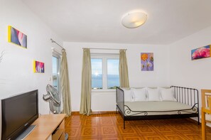A room with a bed, a TV, a fan, and a window with curtains. - Apartments Mrvelj (Jelsa)