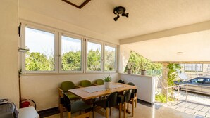 A room with a large table and chairs, a potted plant, and a car parked outside. - Apartments Mrvelj (Jelsa)