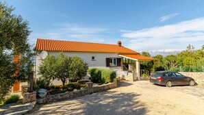 A two-story house with a red-tiled roof, a car parked in the driveway, and a stone wall surrounding the property. - Apartments Mrvelj (Jelsa)