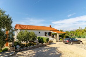 A house with a red-tiled roof, a car parked in front, and a stone wall with greenery around. - Apartments Mrvelj (Jelsa)