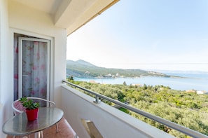 Un balcón con una mesa de vidrio, una planta en maceta y vistas a un lago y montañas.