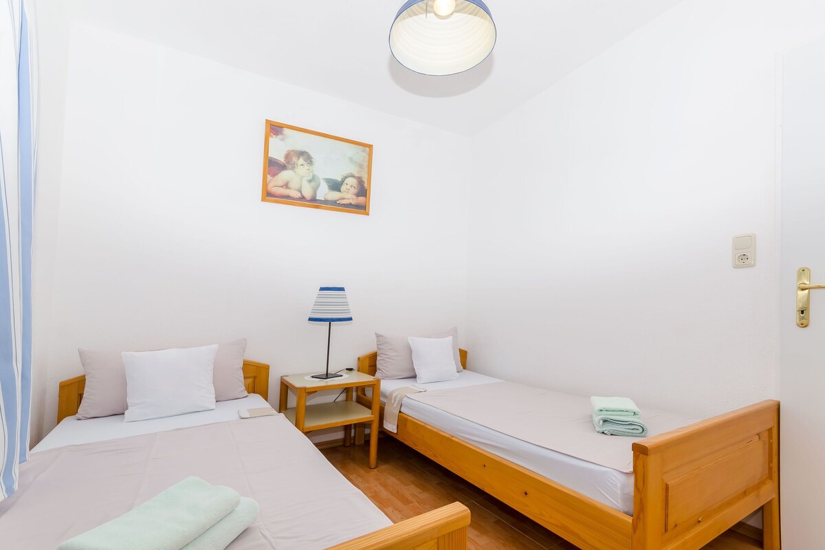 Una habitación con dos camas de madera, una mesita con lámpara y un cuadro en la pared.