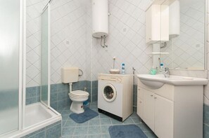Une salle de bain équipée d’une douche, de toilettes, d’un lave-linge et d’un lavabo.