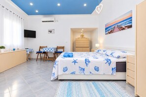 Quarto com cama, escrivaninha, cadeiras, televisão e um quadro.