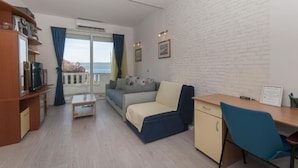 Un soggiorno moderno con divano, scrivania e televisione. È presente un balcone con vista.