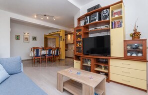 Uma sala de estar com sofá, mesa de centro, televisão e um armário de madeira com prateleiras.