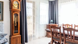 Zona pranzo con tavolo e sedie in legno, un grande orologio a parete e tende leggere.