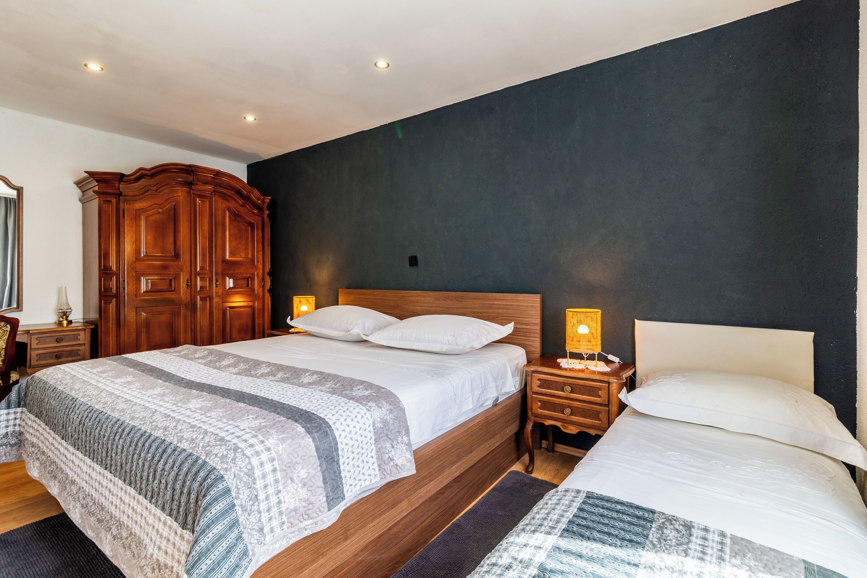 Ein Schlafzimmer mit einem großen Bett, zwei Nachttischen, einem Kleiderschrank und einer dunklen Wand als Blickfang.