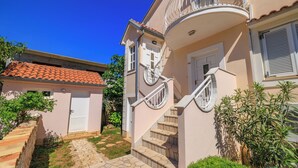 Une maison à deux étages avec un escalier en pierre, un balcon doté d’une balustrade blanche et un toit recouvert de tuiles.