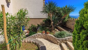 Une cour intérieure avec un chemin en pierre, diverses plantes et une vue sur la mer.