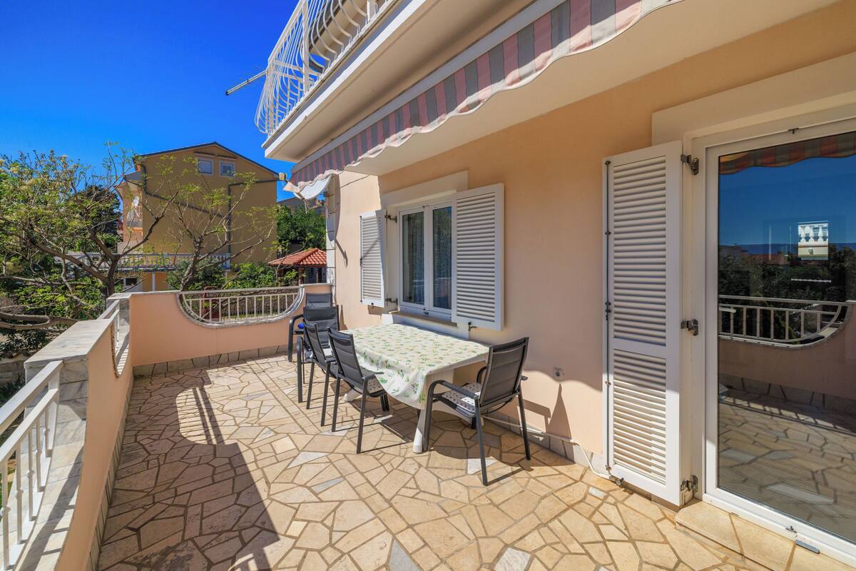 A patio with a table and chairs, a sliding glass door, and a balcony with a railing.
