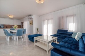 Una sala moderna con un sofá azul, una mesa de centro blanca y una zona de comedor con sillas azules.