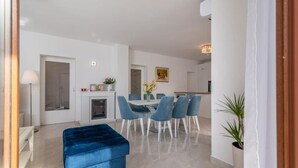 Una sala moderna con un sofá azul, una mesa de comedor con sillas, una chimenea y un pasillo que lleva a otra habitación.