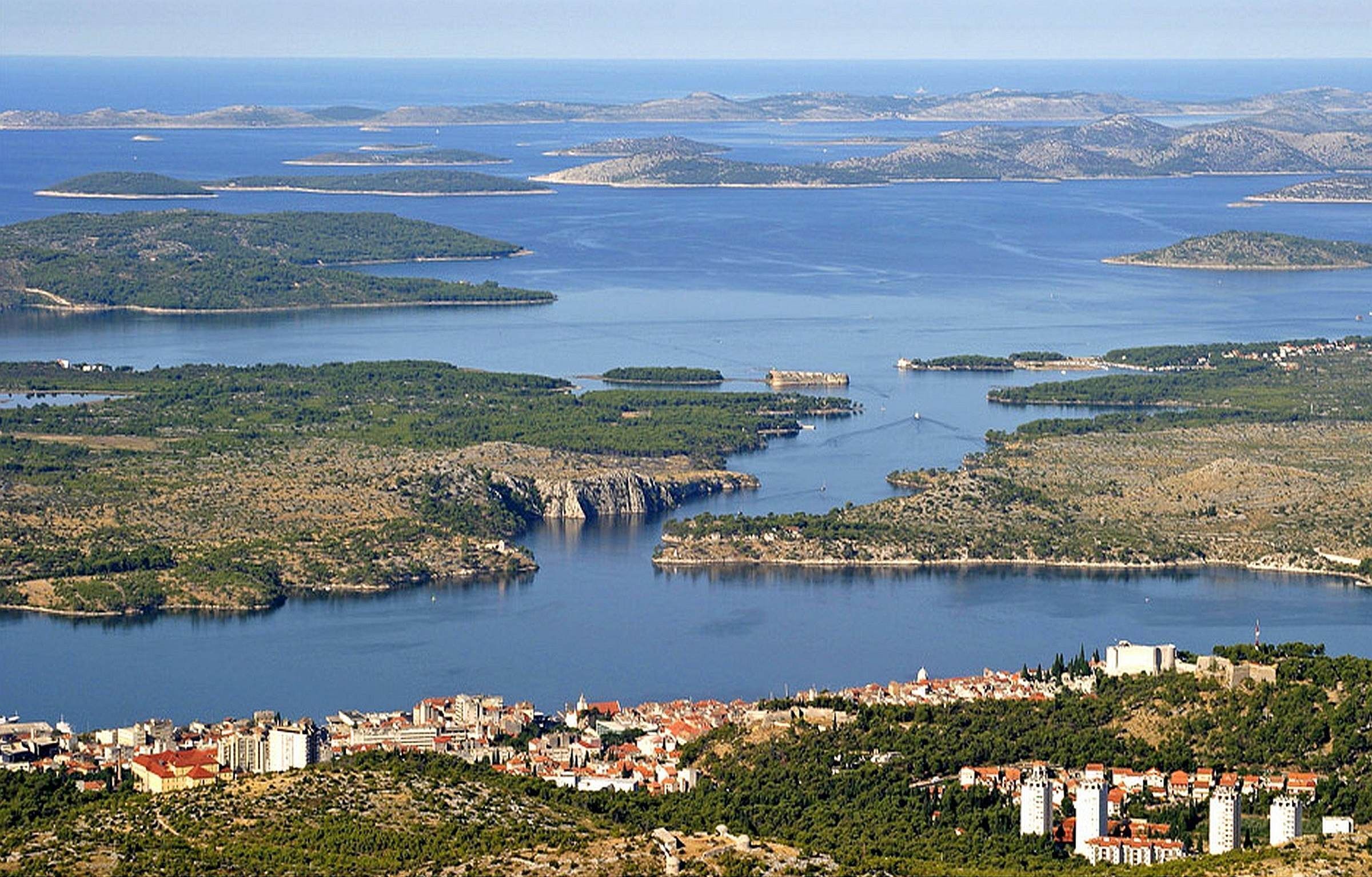 A coastal town with a marina, surrounded by hills and water bodies.