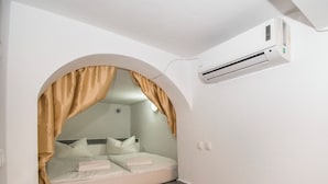 Ein kleiner, schmaler Raum mit einem Bett, einer hölzernen Bank und einer Klimaanlage.