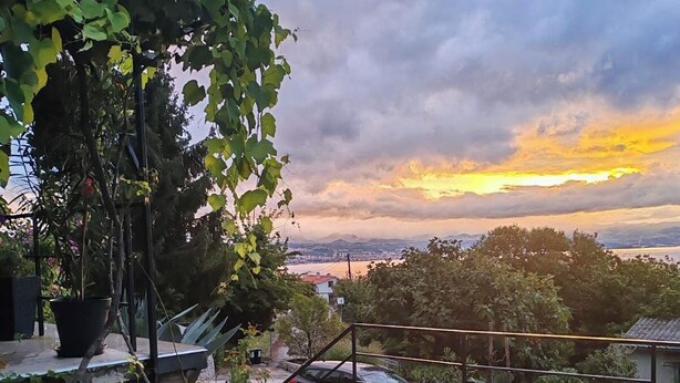 Eine Dachterrasse mit einer Steinmauer, einem Metallgeländer und Blick auf die Skyline im Abendrot.