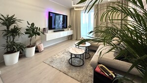 Ein modernes Wohnzimmer mit einem Flachbildfernseher an einer weißen Wand, einer Couch, einem Couchtisch und mehreren Blumentöpfen.