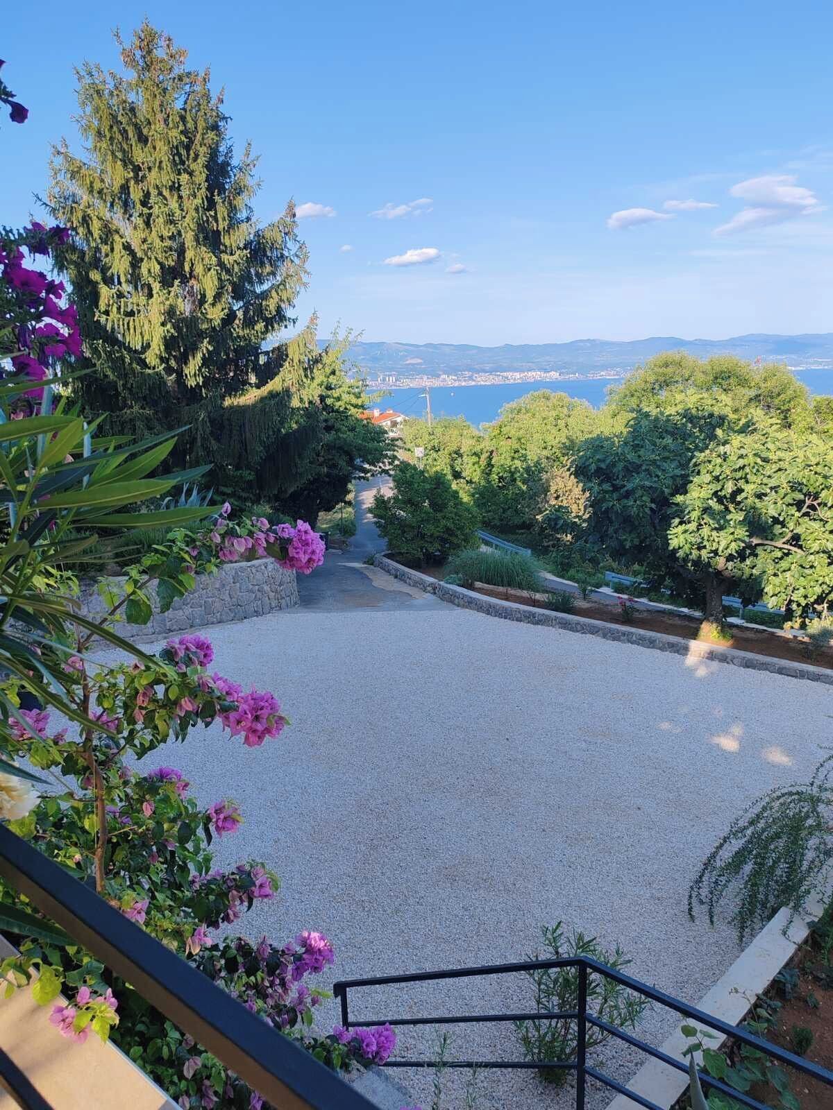 Un sentier de gravier mène à un belvédère offrant une vue panoramique sur une ville côtière et des montagnes.