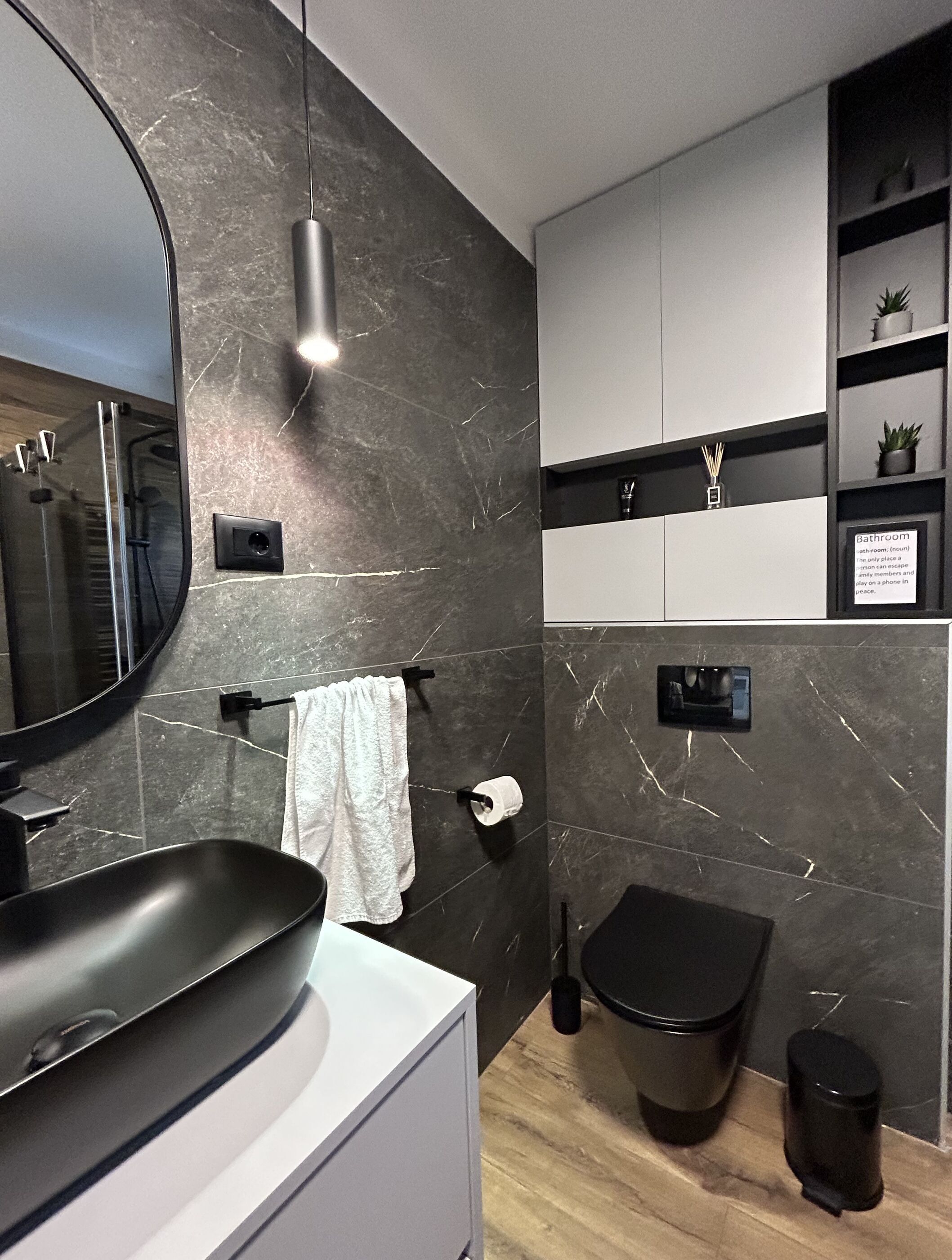 Une salle de bain moderne avec un lavabo noir, un miroir, un porte-serviettes, des toilettes et une étagère contenant des articles de toilette.
