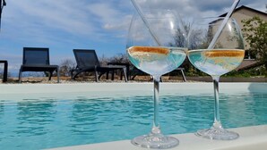 Zwei Gläser mit einer klaren Flüssigkeit und einem Strohhalm, platziert am Pool mit blauem Himmel und Liegestühlen im Hintergrund.