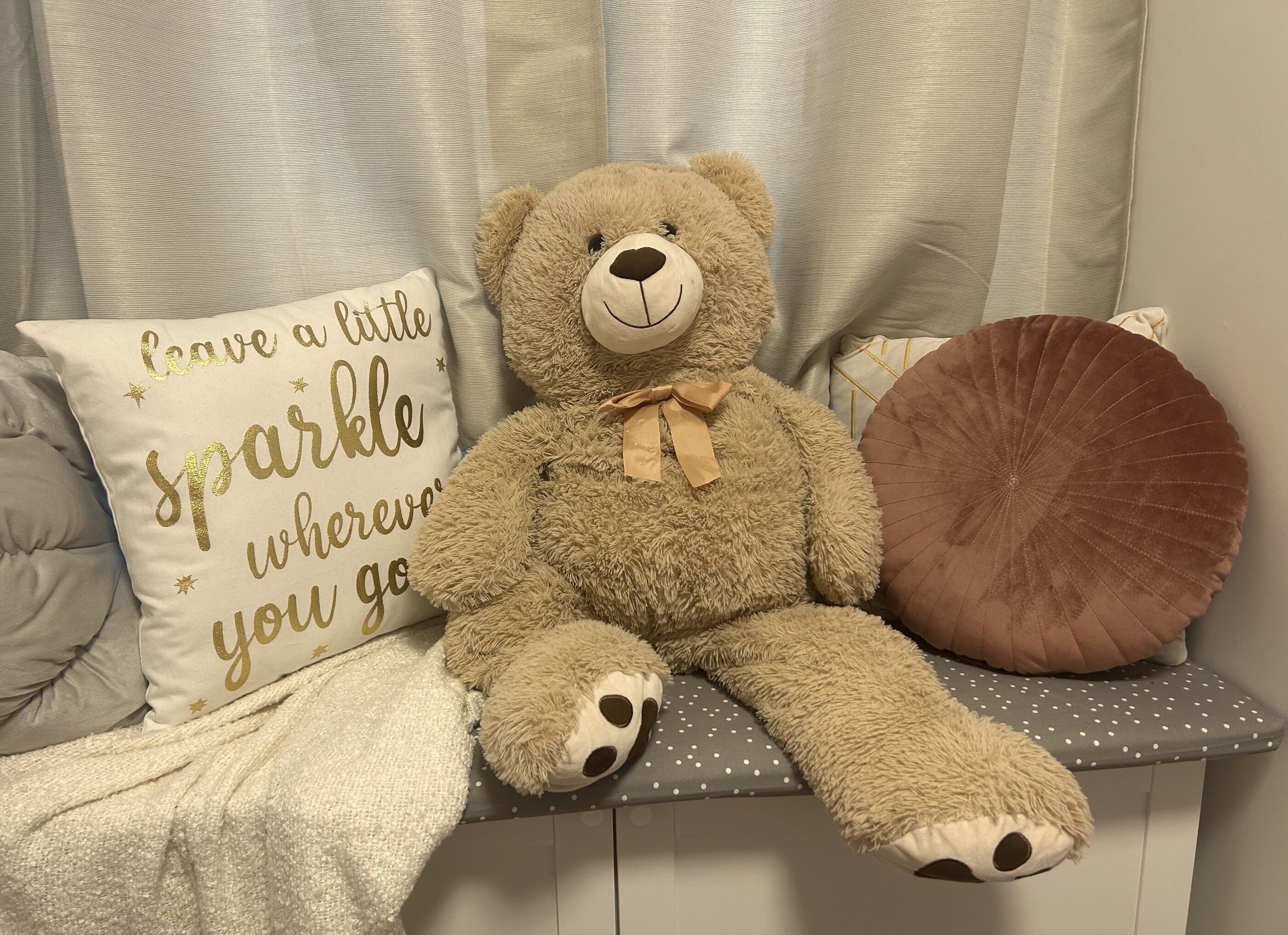Un tenero orsetto di peluche su una panchina con un cuscino che riporta la scritta: “Lascia una scia di magia ovunque tu vada.”