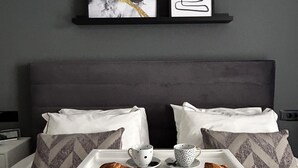 Ein ordentlich bezogenes Bett mit zwei Kissen, ein Tablett mit Croissants und Tassen sowie zwei gerahmte Kunstwerke an der Wand.