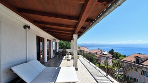 Uma varanda com sofá de vime e uma mesa, com vista panorâmica para o mar e edifícios.