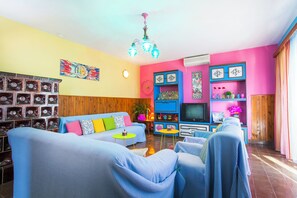 Un soggiorno con divano, poltrone, televisore e parete decorativa con mensole.