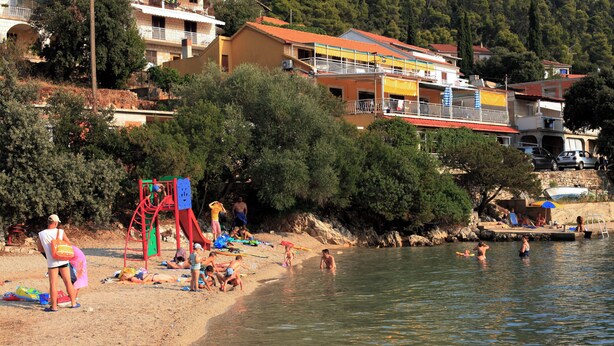 A beach with people sunbathing and swimming, surrounded by houses and trees. - Apartment Colorful (Smokvica)