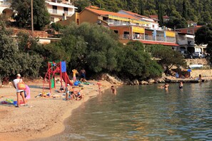 A beach with people sunbathing, a playground, and a boat docked near the shore. - Apartment Colorful (Smokvica)