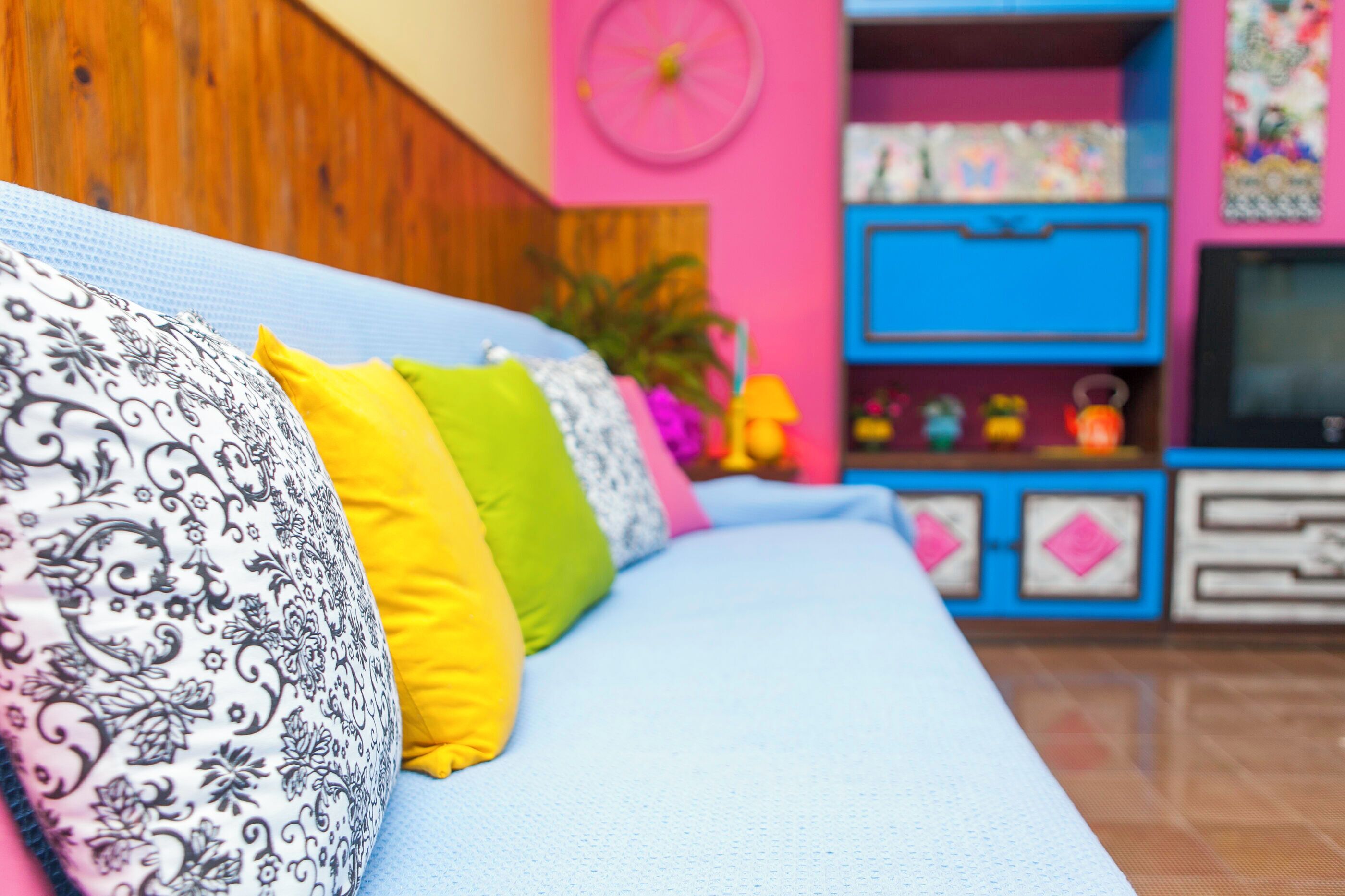 A sofa with patterned and solid-colored cushions, a wooden wall, and a blue cabinet with drawers.