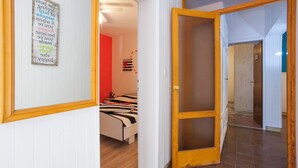 A hotel room with a bed, a wooden door, and a hallway leading to another room. - Apartment Colorful (Smokvica)