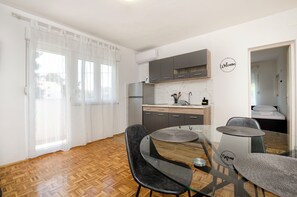 A compact kitchen with modern appliances, a dining area with two chairs, and a bed in the adjacent room. - Apartments and Rooms Jengic (Vodice)