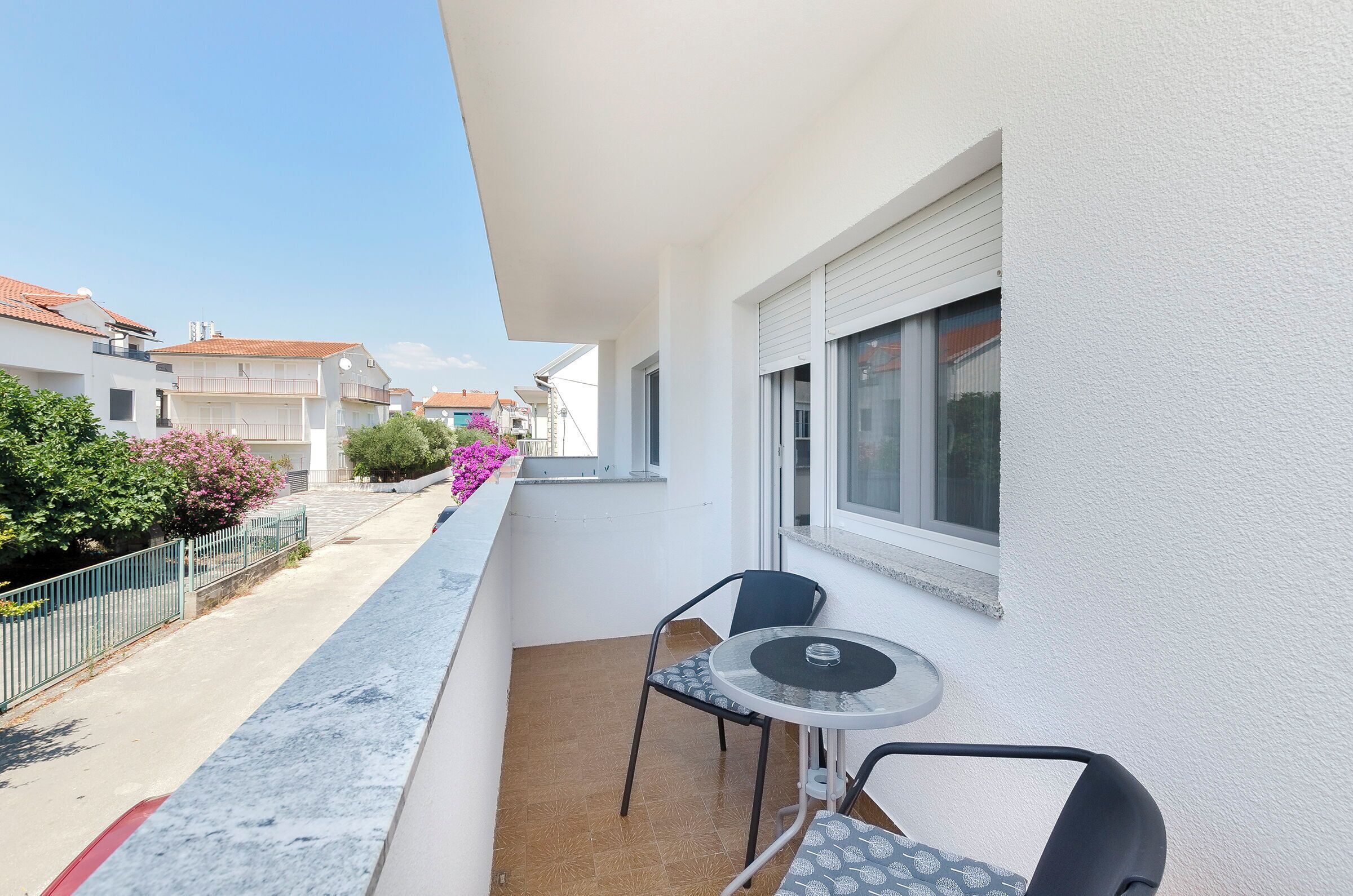 A balcony with a table and chairs, a window, and a view of neighboring buildings.