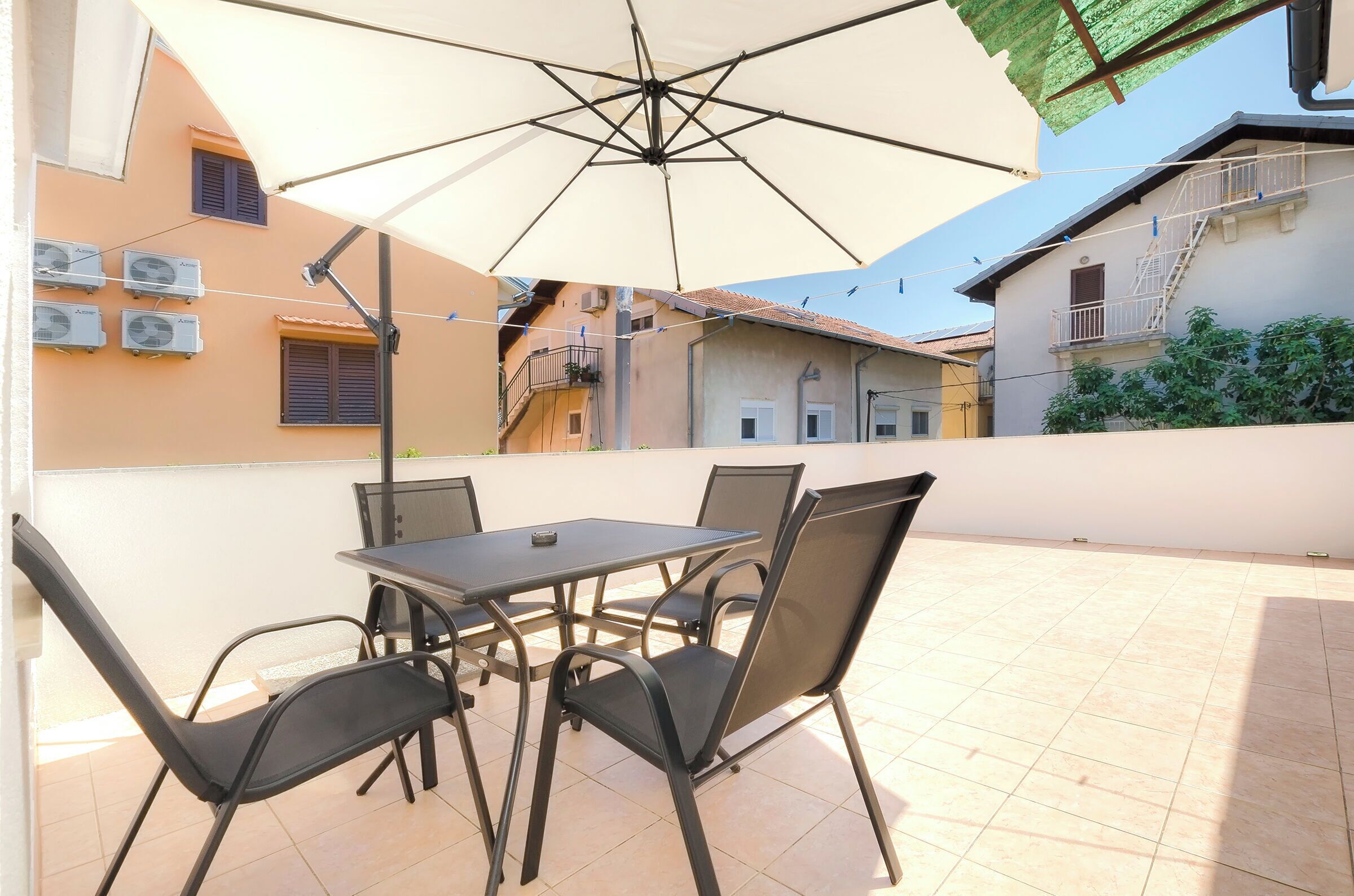 Une terrasse extérieure avec une table et des chaises, un parasol et des unités de climatisation installées sur le bâtiment.