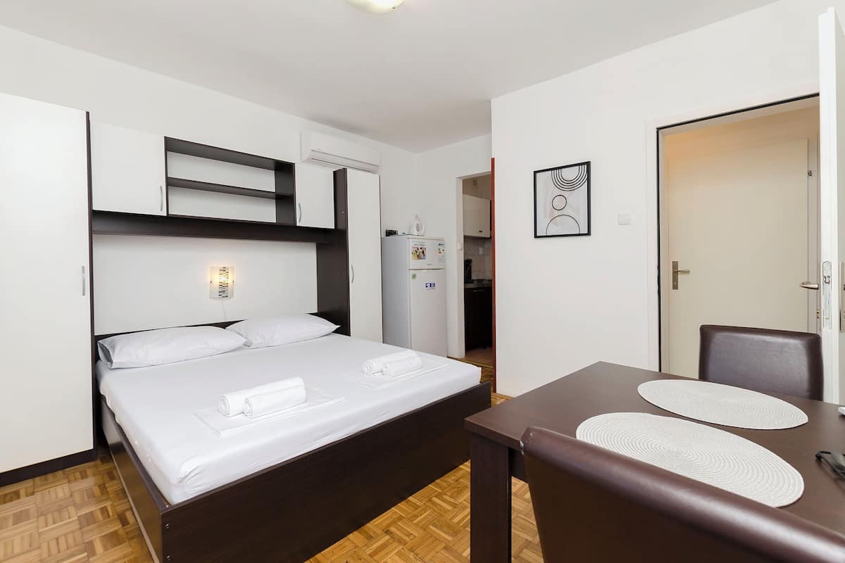 Una habitación de hotel con cama, una mesita, un refrigerador y una puerta.